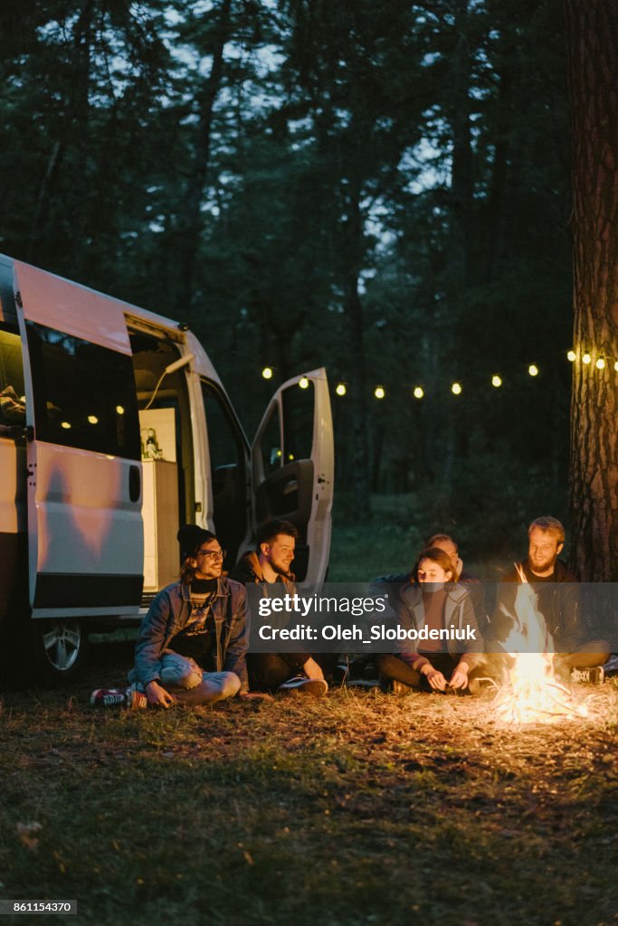 Friends sitting near campfire in the forest near the camper van