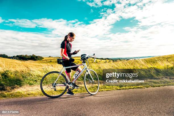 sportliche frau am racing fahrrad nutzt handy während dem training auf landstraße - denmark cycling stock-fotos und bilder