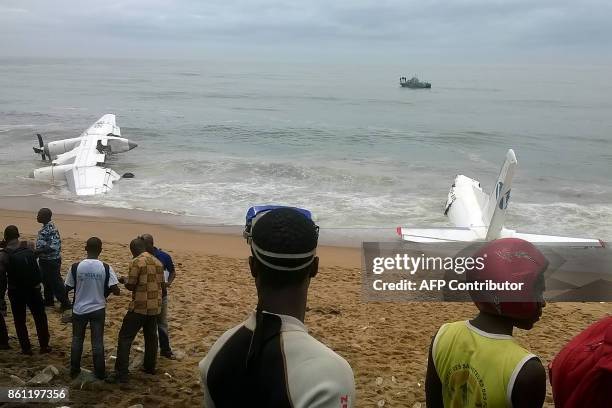 Picture taken on October 14, 2017 with a mobile phone shows people looking at the wreckage of a plane that crashed off Ivory Coast today, killing at...