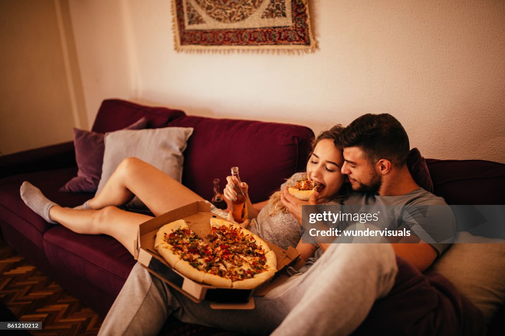 Young hipster couple relaxing on the sofa eating pizza
