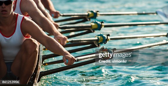Four male athletes rowing across lake in late afternoon Four male athletes rowing across lake in late afternoon