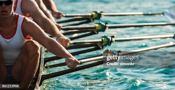 four male athletes rowing across lake in late afternoon - rowing competition stock pictures, royalty-free photos & images