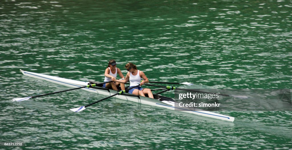 Två kvinnliga idrottare rodd över sjön i sena eftermiddagen