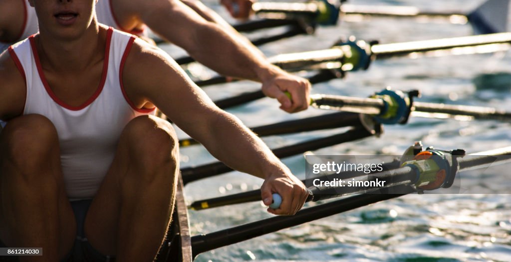 Three male athletes rowing across lake in late afternoon