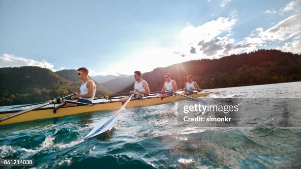 quatre athlètes masculins d’aviron sur le lac en fin d’après-midi - sweep rowing photos et images de collection