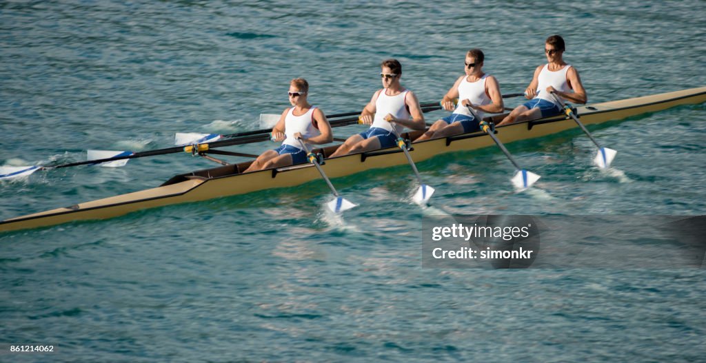 Four male athletes rowing across lake in late afternoon