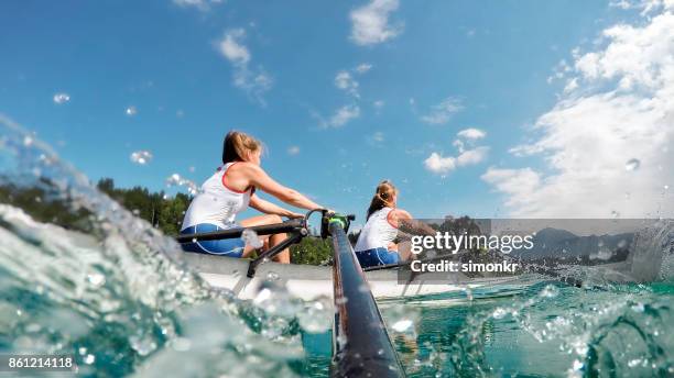 two female athletes rowing across lake in late afternoon - rowing team stock pictures, royalty-free photos & images