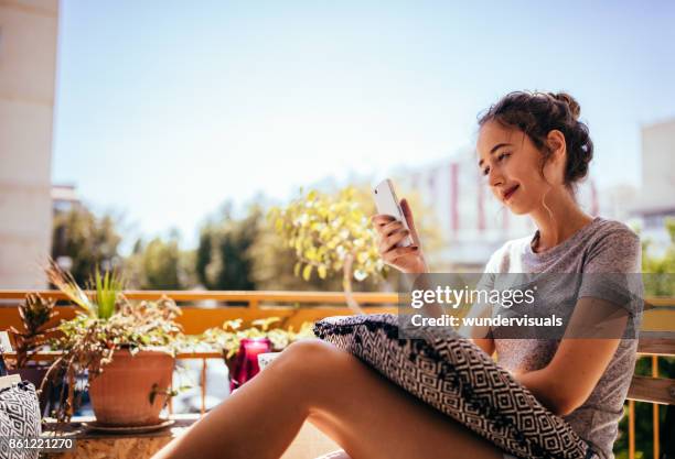 mooie jonge hipster vrouw zit op balkon met smartphone - bel appartement stockfoto's en -beelden