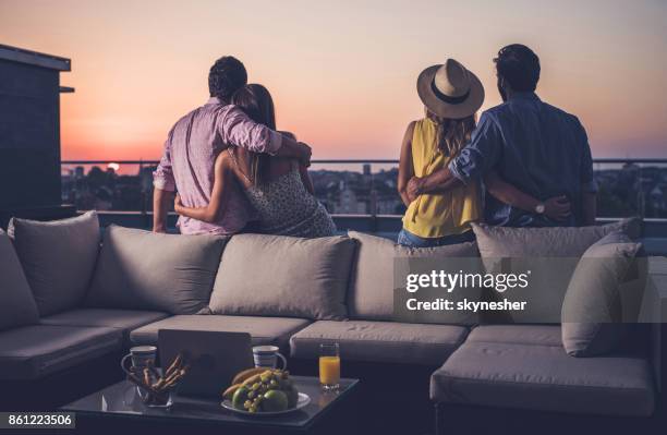 rear view of two embraced couples looking at sunrise from a penthouse terrace. - double date stock pictures, royalty-free photos & images
