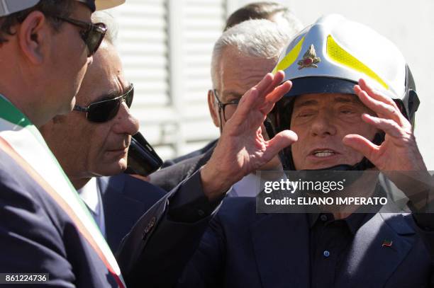 Italian former Prime Minister and president of right-wing party Forza Italia, Silvio Berlusconi wears an helmet of fireman on October 14, 2017 as he...