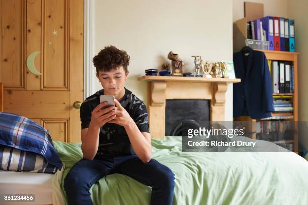 teenage boy in his bedroom texting on smartphone - boy sitting on bed stock-fotos und bilder