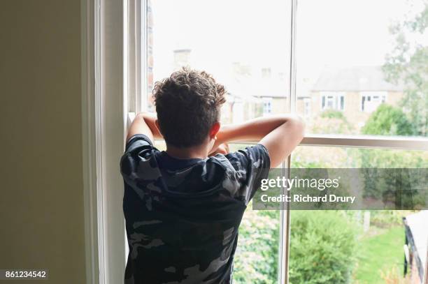 teenage boy looking out of bedroom window - männlicher teenager stock-fotos und bilder