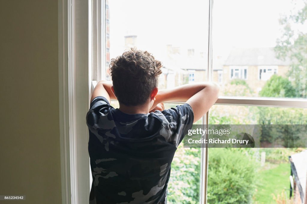 Teenage boy looking out of bedroom window
