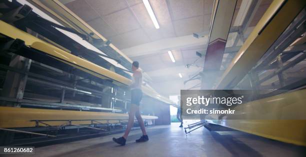 deux athlètes masculins transportant balayage rame bateau dans une remise à bateaux - sweep rowing photos et images de collection