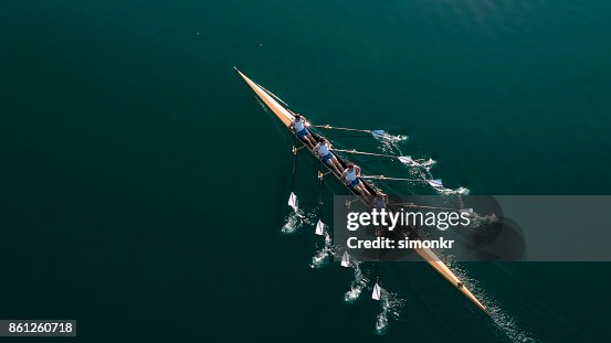 Four male athletes sculling on lake in sunshine