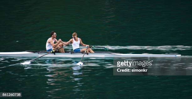 two male athletes rowing across lake in late afternoon - sweep rowing stock pictures, royalty-free photos & images