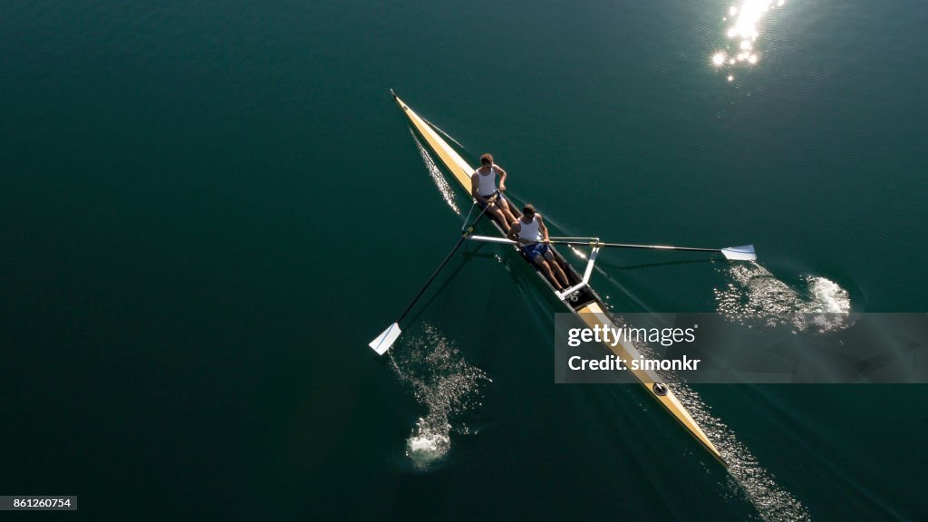 Two male athletes sculling on lake in sunshine