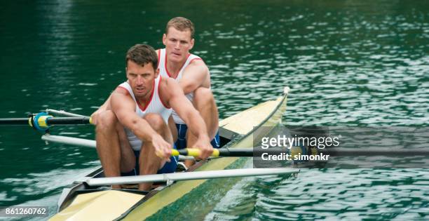 two male athletes rowing across lake in late afternoon - sweep rowing stock pictures, royalty-free photos & images