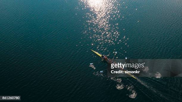 onze mannelijke atleten sculling op meer in de zon - wrikken roeisport stockfoto's en -beelden