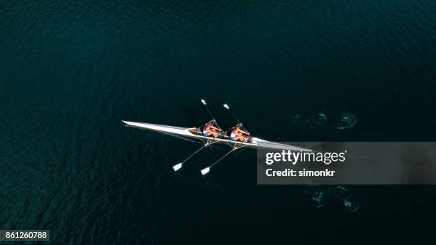 due atlete che sculling sul lago sotto il sole - remo foto e immagini stock