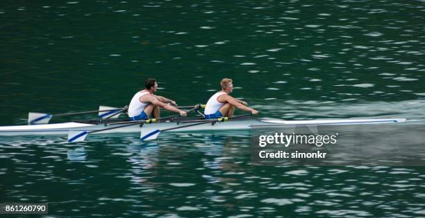 dos atletas masculinos remo lago tarde - remo de punta fotografías e imágenes de stock