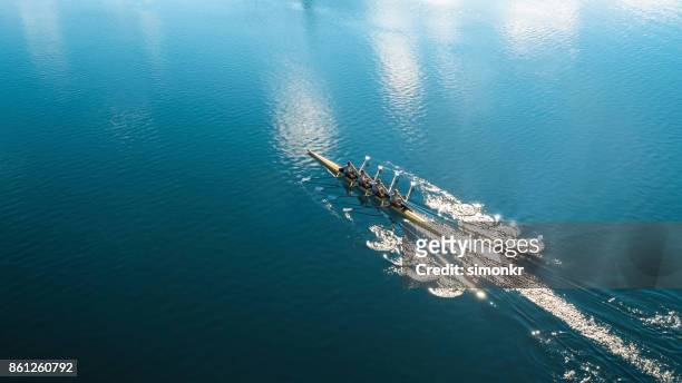 quattro atleti maschi che sculling sul lago sotto il sole - rowing foto e immagini stock