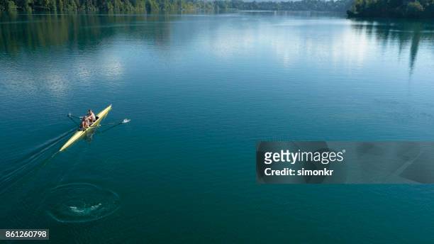 due atleti maschi che sculling sul lago sotto il sole - sweep rowing foto e immagini stock