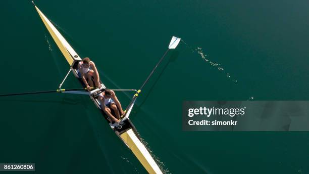 twee mannelijke atleten sculling op meer in de zon - wrikken roeisport stockfoto's en -beelden