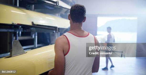 two male athletes carrying sweep oar boat into boathouse - sweep rowing stock pictures, royalty-free photos & images