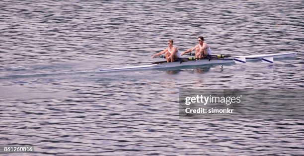 two male athletes rowing across lake in late afternoon - sweep rowing stock pictures, royalty-free photos & images