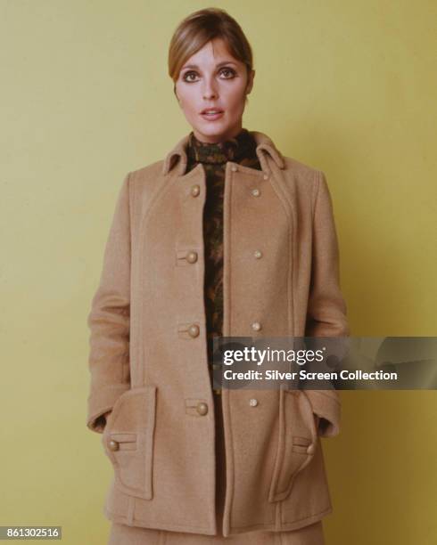 Portrait of American model and actress Sharon Tate , her hands in her coat-pockets, as she poses against a yellow background, late 1960s.