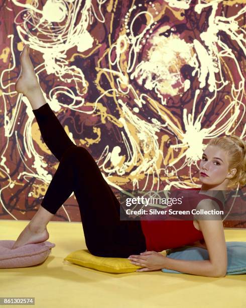 Portrait of American actress Yvette Mimieux as she reclines on several cushions on the floor, one barefoot leg in the air, early 1960s.