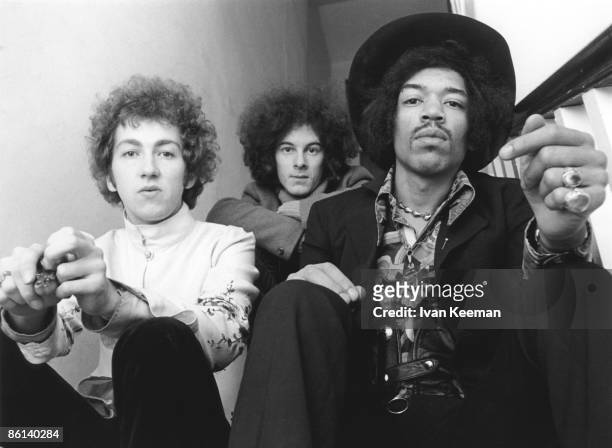 American guitarist and singer Jimi Hendrix seated on right with, on left, drummer Mitch Mitchell and, behind in centre, bassist Noel Redding of the...