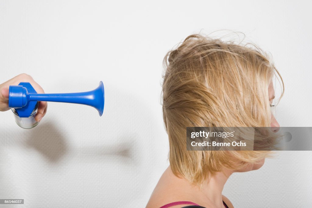 A woman with an air horn being blown at the back of her head