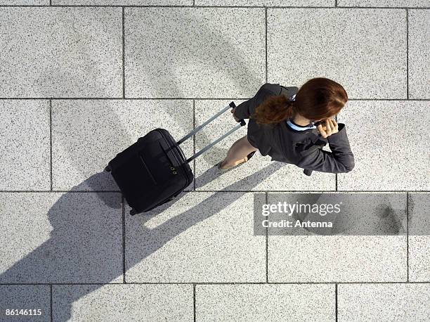 a businesswoman pulling a suitcase and talking on her mobile phone - suitcase from above imagens e fotografias de stock