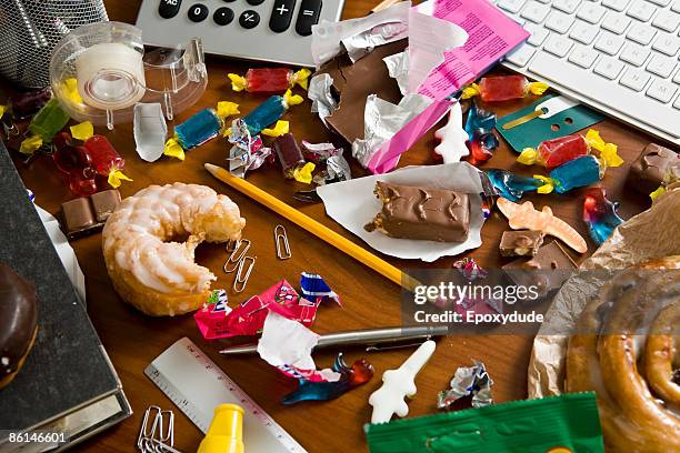 an office desk cluttered with candy and sweets - stress und essen stock-fotos und bilder