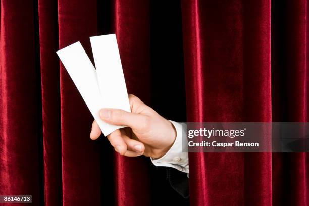 a hand holding two tickets through a red velvet curtain - holding two things stock pictures, royalty-free photos & images