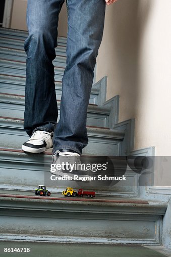 A man walking down stairs about to step on toy cars A man walking down stairs about to step on toy cars