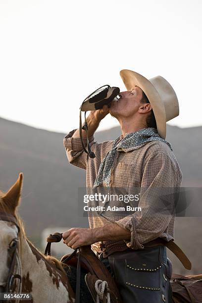 a cowboy sitting on a horse and drinking from a hip flask - flachmann stock-fotos und bilder