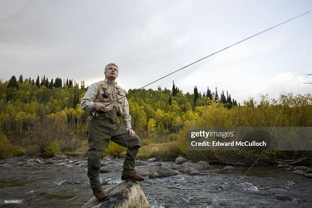 A man standing on a rock while fly fishing in a river