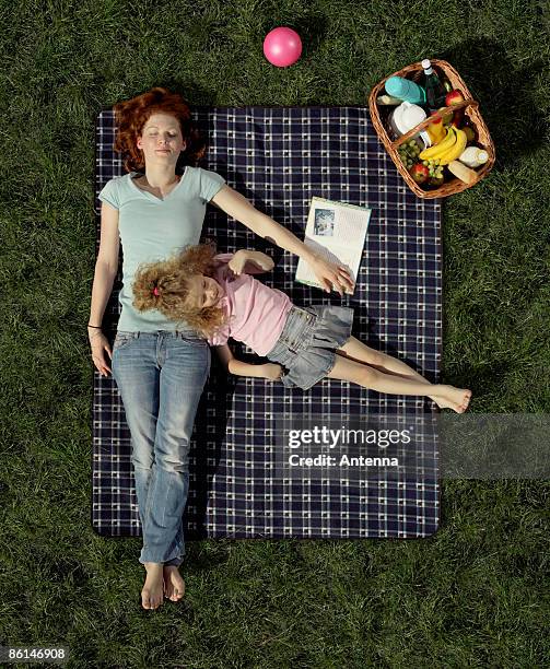 a mother and daughter lying on a blanket on the grass resting - picnic blanket stockfoto's en -beelden