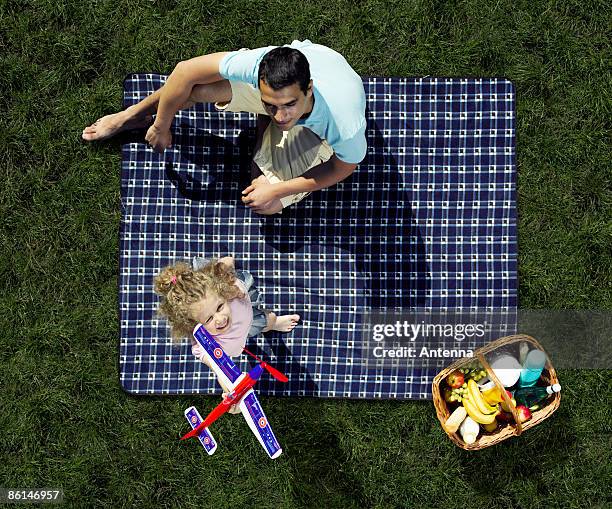 a father and daughter having a picnic and playing with a toy airplane - manta de picnic fotografías e imágenes de stock