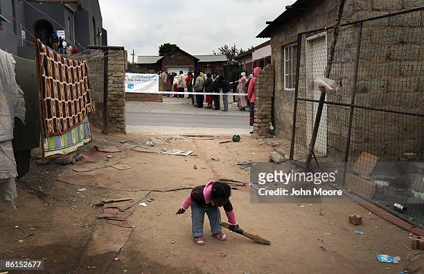 Child sweeps her family's driveway as voters wait for hours in a long queue to cast their ballots in national elections April 22, 2009 in Alexandra...