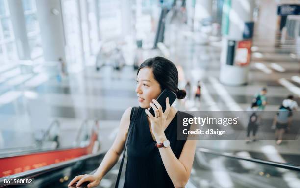 smart young lady talking on smartphone on escalators - airport business meeting stock pictures, royalty-free photos & images