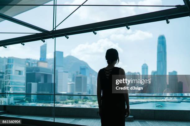 silhouette of woman looking through window at prosperous skyline of hong kong - self doubt ストックフォトと画像