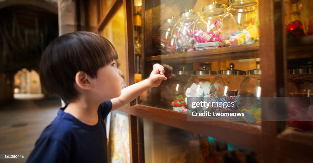 East asian young boy looking at colourful candy jars.