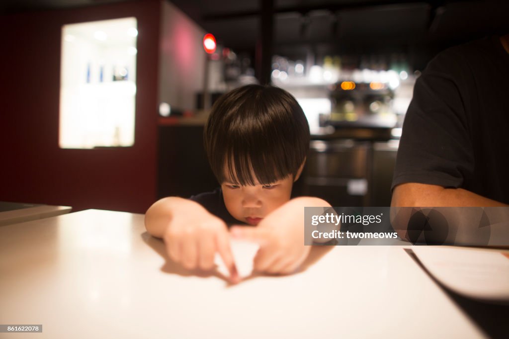 East asian young boy looking bored by waiting time in restaurant.