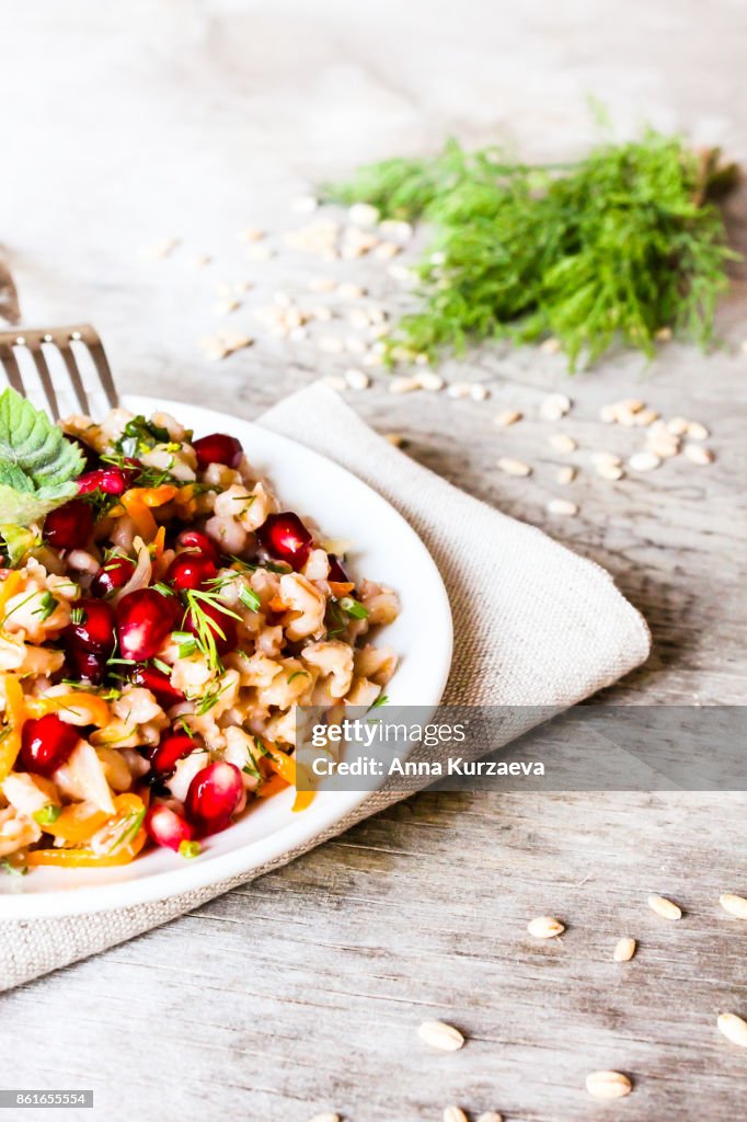 Warm salad with barley, carrot, onion, pomegranate seeds and fresh mint in a plate on a wooden table, selective focus