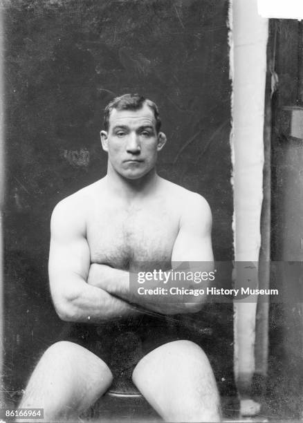 Three-quarter length portrait of Tom "Sailor" Sharkey, noted boxer, sitting with arms folded, facing the camera, against a dark backdrop in a...