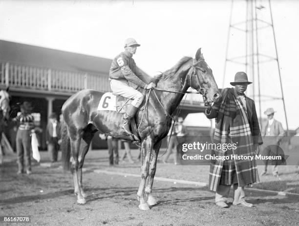 Image of with jockey mounted and an African American handler holding its bridle, standing in paddock at Worth Race Track in Worth, Illinois, 1902.